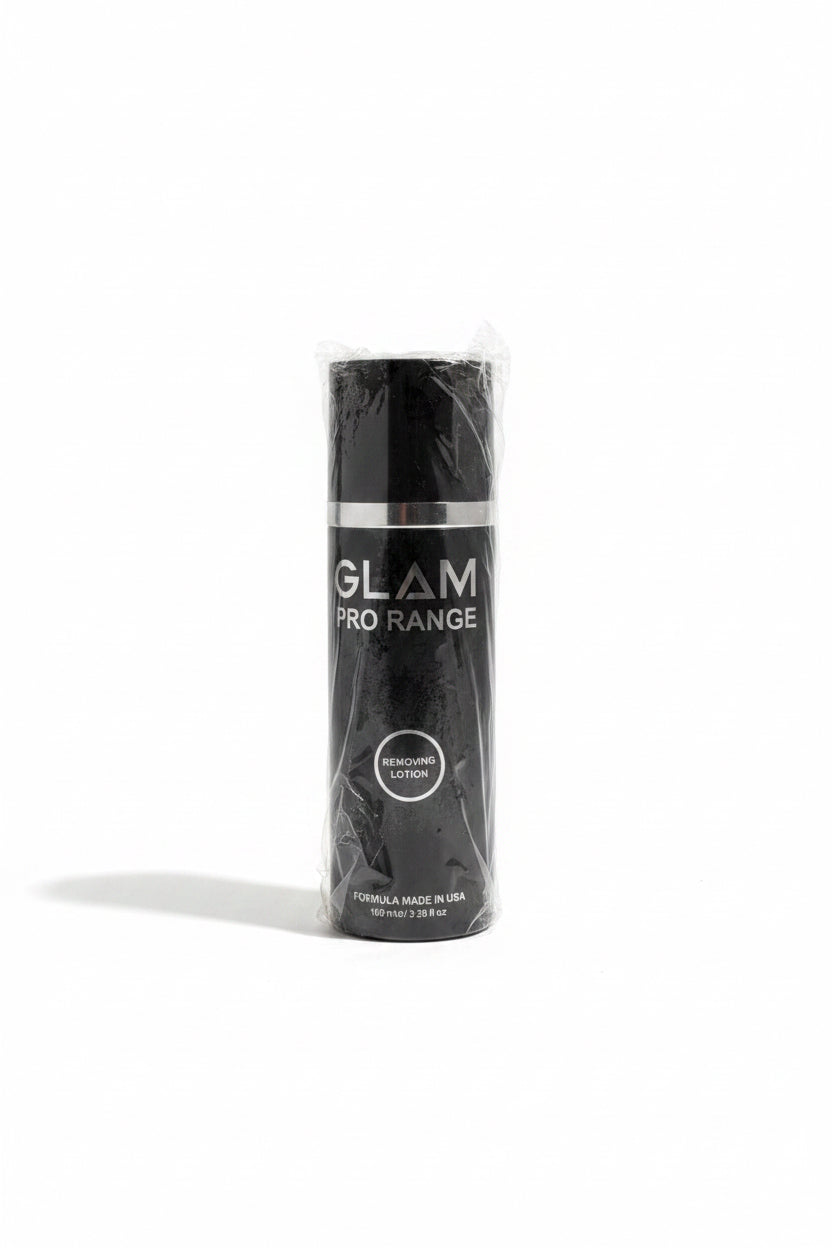 A black cylindrical bottle of Glam Pro Range Dehydrating Lotion wrapped in clear plastic, placed on top of an open laptop on a desk with a notebook and other office items in the background.
