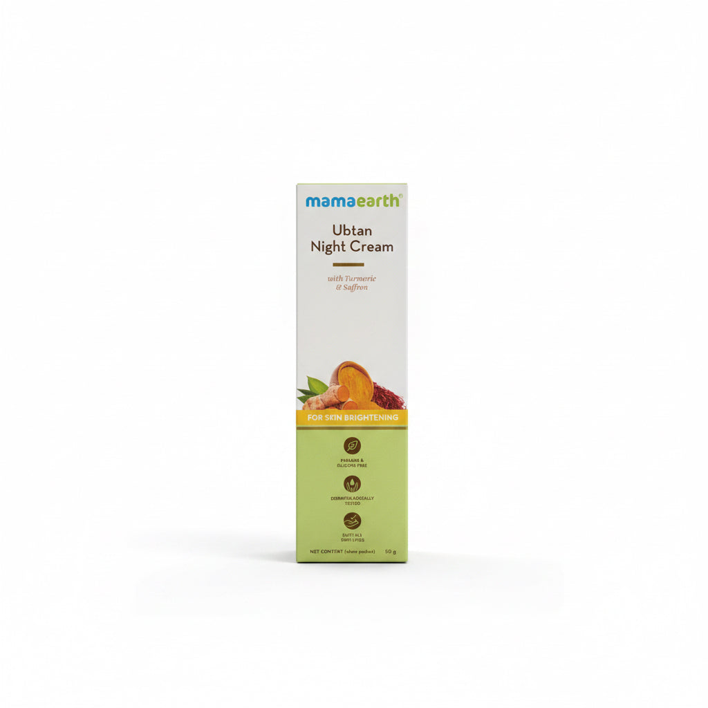 A box of Mama Earth Ubtan Night Cream stands upright on a desk in front of an open laptop. The packaging is cream and light green with orange and yellow accents, and the brand name 'mamaearth' is clearly visible at the top.