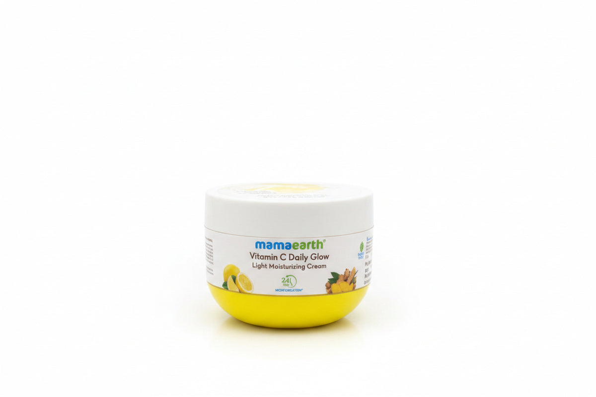 A jar of Mama Earth Vitamin C Daily Glow Light Moisturizing Cream sits on a dark counter next to a laptop and a green plastic basket.