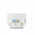 A white jar of Mama Earth Rice Dewy Bright Light Moisturizing Cream placed on a dark surface, with a green plastic basket and a light-colored wall in the background.