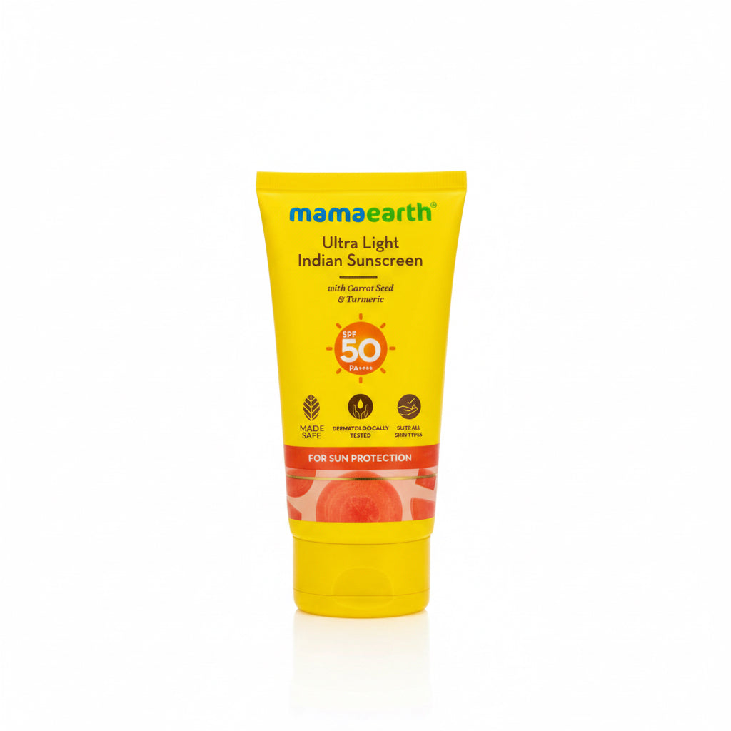 A yellow squeeze tube of Mamaearth Ultra Light Indian Sunscreen SPF 50+ with Carrot Seed & Turmeric, placed on a dark surface in front of a green plastic basket.