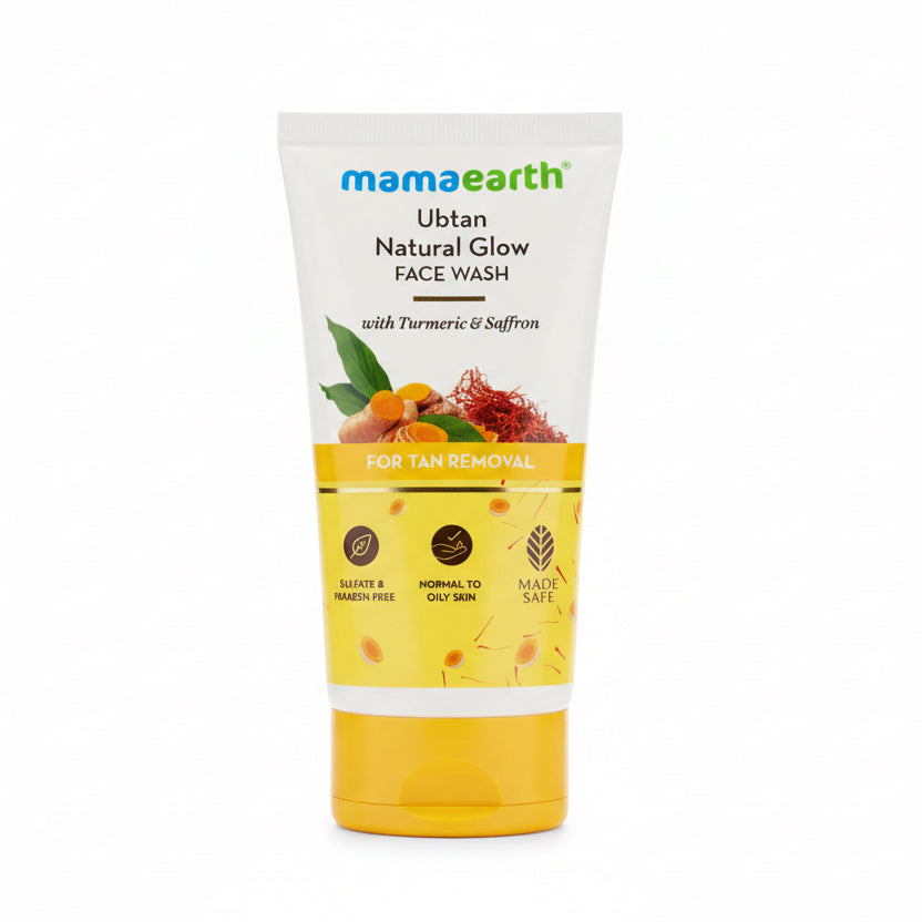 A tube of Mama Earth Ubtan Natural Glow Face Wash standing on a desk in front of an open laptop, with a calculator and a blurred person in the background.