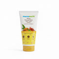 A tube of Mamaearth Ubtan Natural Glow Face Wash standing on a laptop keyboard in a workspace setting. The product packaging is cream and yellow with orange and red botanical illustrations, and the Mamaearth brand name is clearly visible.