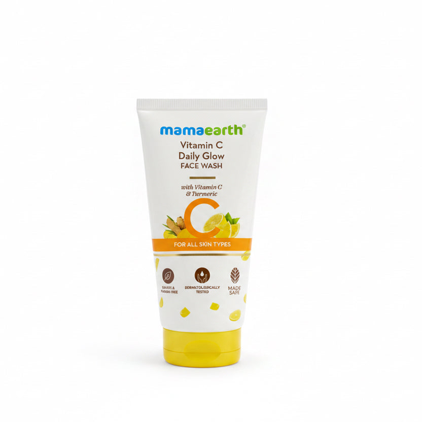 A tube of Mama Earth Vitamin C Daily Glow Face Wash standing upright on a black surface in front of a teal plastic basket.