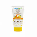 A tube of Mama Earth Vitamin C Daily Glow Face Wash standing on a dark surface, with a laptop and a green basket visible in the background.