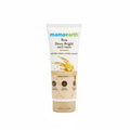 A tube of Mama Earth Rice Dewy Bright Face Wash stands on a counter in front of a green plastic basket, with a laptop and another box visible in the background.