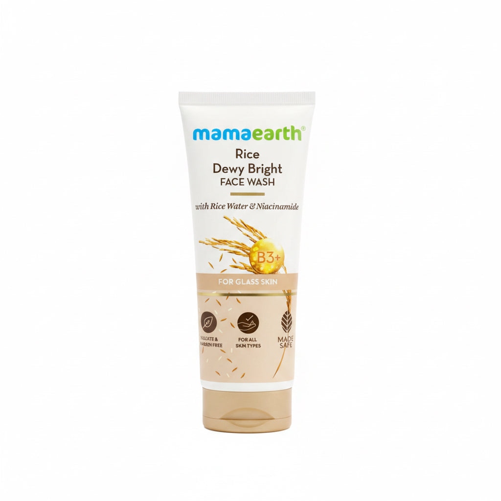 A tube of Mama Earth Rice Dewy Bright Face Wash stands on a counter in front of a green plastic basket, with a laptop and another box visible in the background.