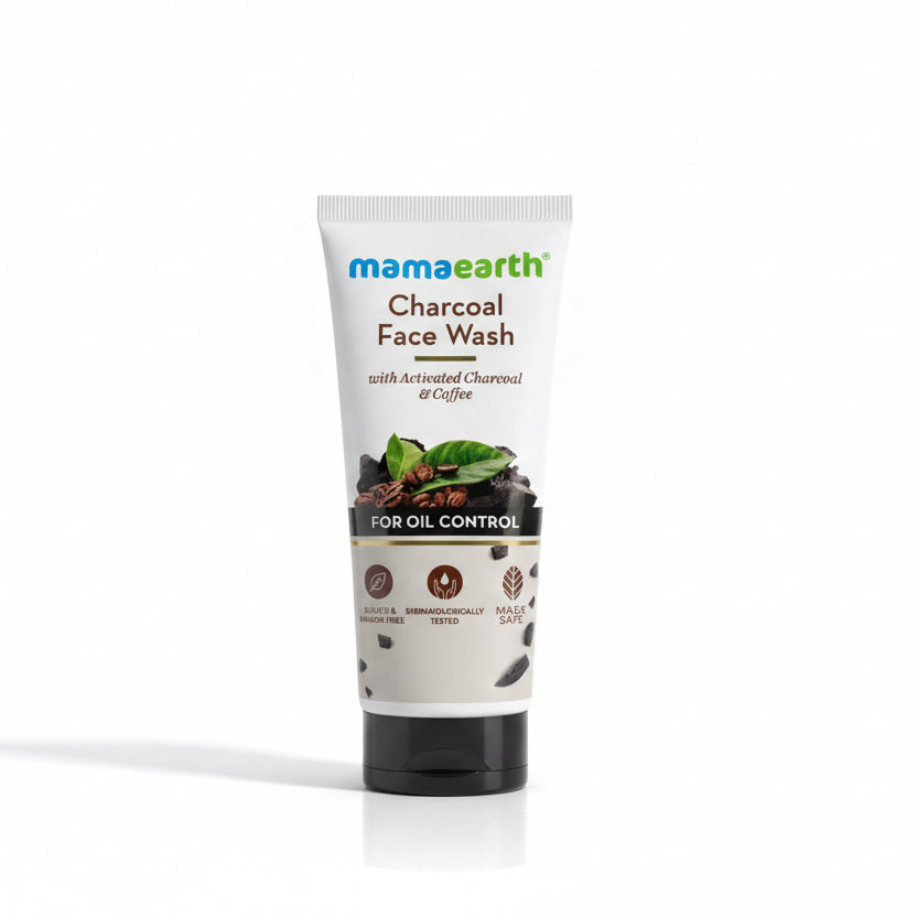 A tube of Mama Earth Charcoal Face Wash standing on a dark tabletop, with a laptop partially visible on the right and a real indoor environment in the background.