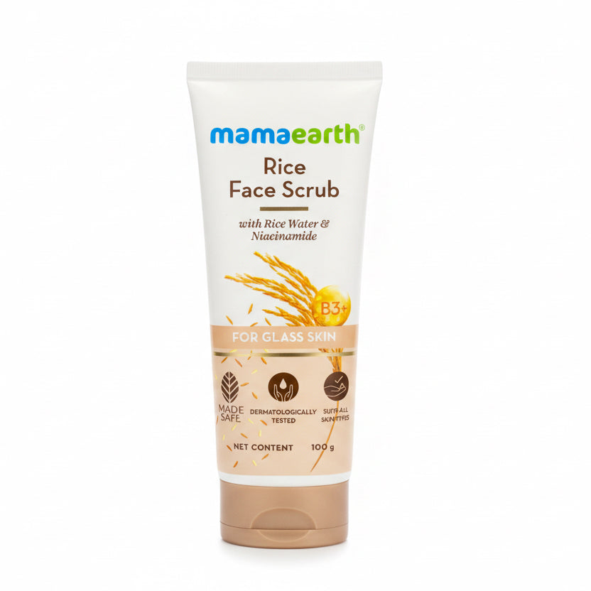 A 100g tube of Mamaearth Rice Face Scrub for glass skin, standing on a dark countertop. The packaging is white with green and blue branding, brown text, and illustrations of rice grains.