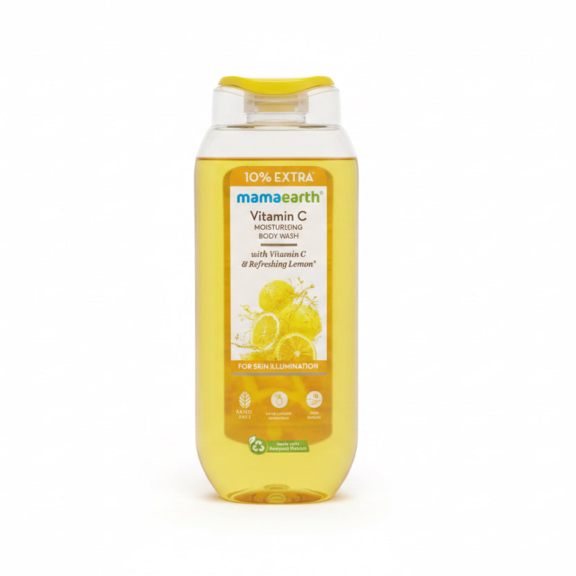 A bottle of Mamearth Vitamin C Moisturizing Body Wash with yellow liquid inside, placed on top of an open laptop on a red surface with other toiletries in the background.