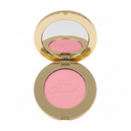 A close-up of a hand holding an open round makeup compact containing pink pressed powder with the brand name 'Too Faced' embossed on it. The compact has a gold-toned rim and a mirror on the inside lid.