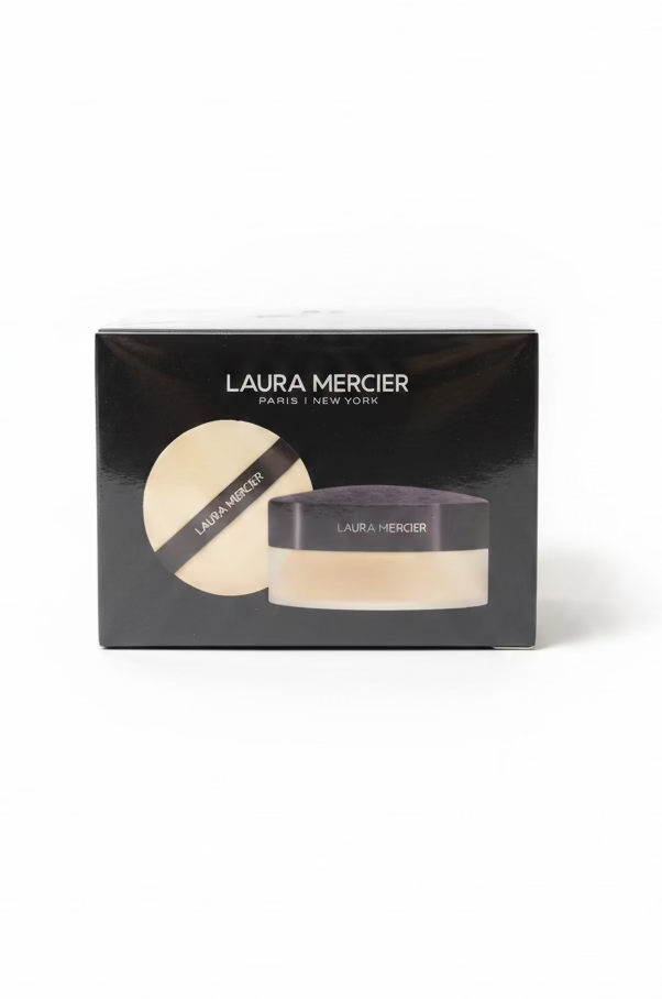 A boxed Laura Mercier powder foundation product sits on a glass shelf in a retail or salon setting, with a laptop and other cosmetic items blurred in the background.