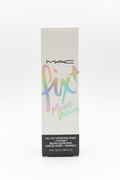 A box of MAC Fix Magic Radian All-Day Hydrating Spray standing on a glass display counter in a retail store. The packaging is white with a holographic pastel 'fix' script and a black text block at the bottom.
