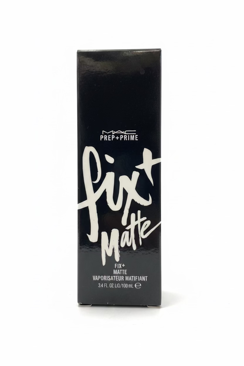 A black rectangular box of MAC Prep+Prime Fix + Matte liquid lipstick stands on a glass display shelf in a retail store. The box features white text and is surrounded by shelves of cosmetics and a laptop in the background.