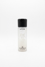 A bottle of MAC Prep + Prime Pix Matte liquid makeup foundation placed on a glass counter in a retail store, with a laptop and shelves of products blurred in the background.