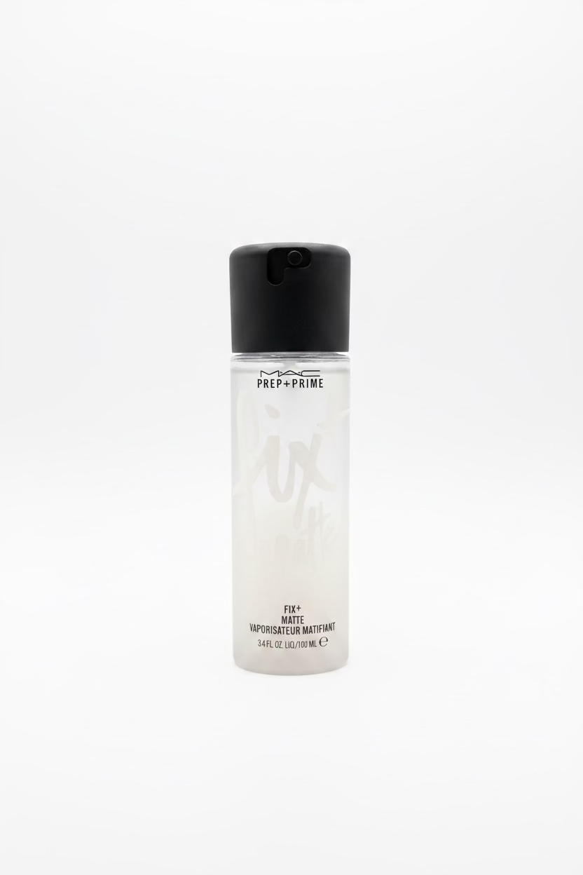 A bottle of MAC Prep + Prime Pix Matte liquid makeup foundation placed on a glass counter in a retail store, with a laptop and shelves of products blurred in the background.