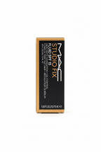 A box of MAC Studio Fix Fluid SPF 45 foundation, shown standing upright on a glass counter in a store setting with a blurred person's hand visible on the left.