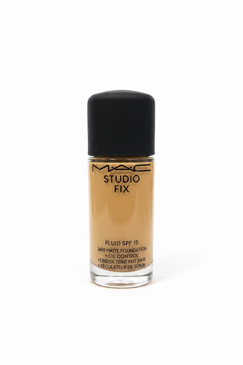 A bottle of MAC Studio Fix Fluid SPF 15 liquid foundation with a black cap, placed on a glass display counter in a retail store setting with a laptop and other products blurred in the background.