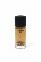 A bottle of MAC Studio Fix Fluid SPF 15 liquid foundation with a black cap, placed on a glass display counter in a retail store setting with a laptop and other products blurred in the background.