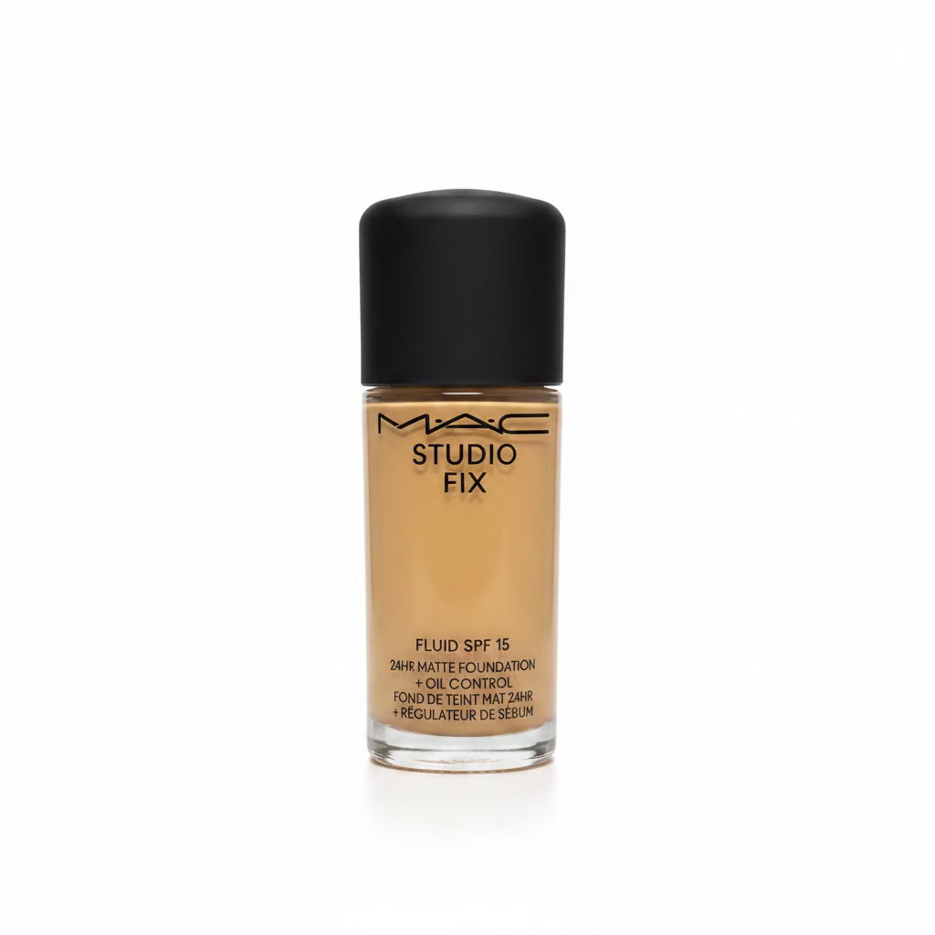 A bottle of MAC Studio Fix Fluid SPF 15 liquid matte foundation with a black cap, placed on a glass counter in a retail or studio setting with a laptop and boxes blurred in the background.